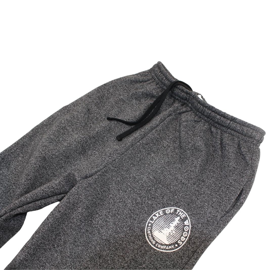 A pair of dark grey sweatpants with a Lake of the Woods Clothing Company logo design printed on the top left front leg. These sweatpants are made in Canada and are fit for men and women