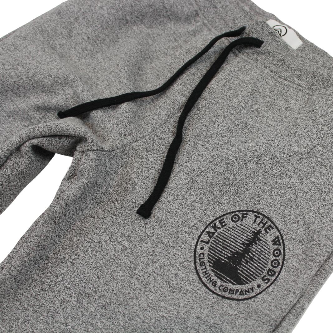 A pair of dark grey sweatpants with a Lake of the Woods Clothing Company logo design printed on the top left front leg. These sweatpants are made in Canada and are fit for women.