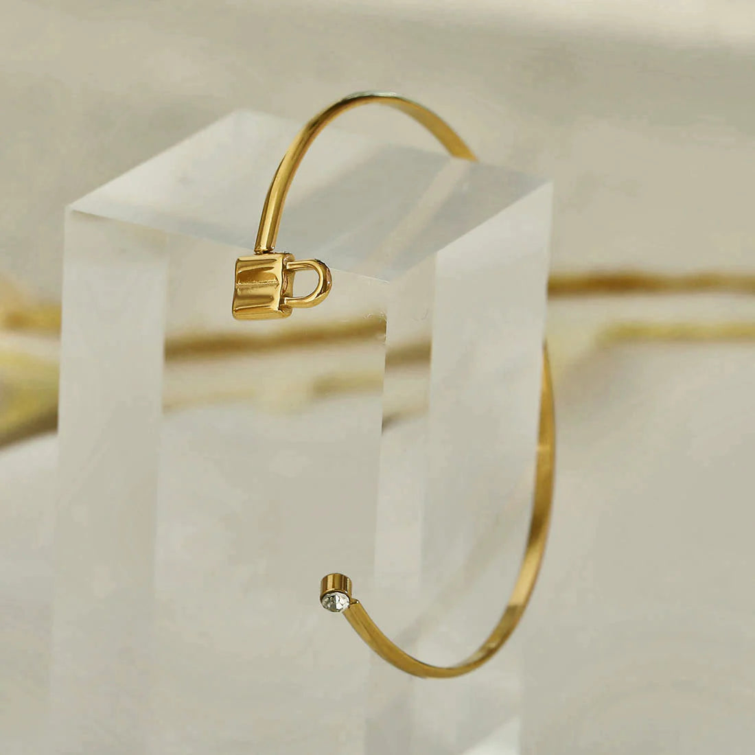 Hackney jewelry featuring an open adjustable gold bracelet with a sparkling gemstone on one end and a lock on the other.