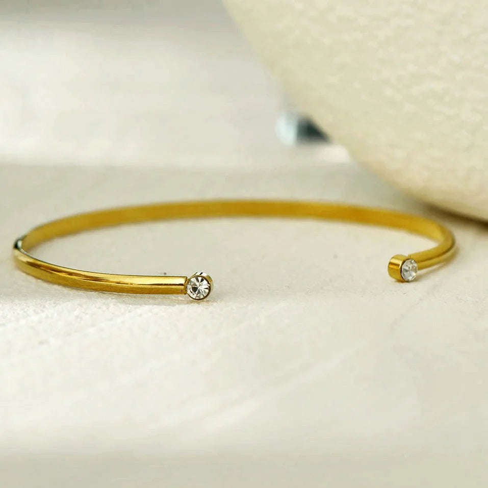 Hackney jewelry featuring an open adjustable gold bracelet with a gemstone on either opening end.