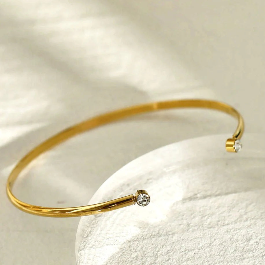 Hackney jewelry featuring an open adjustable gold bracelet with a gemstone on either opening end.