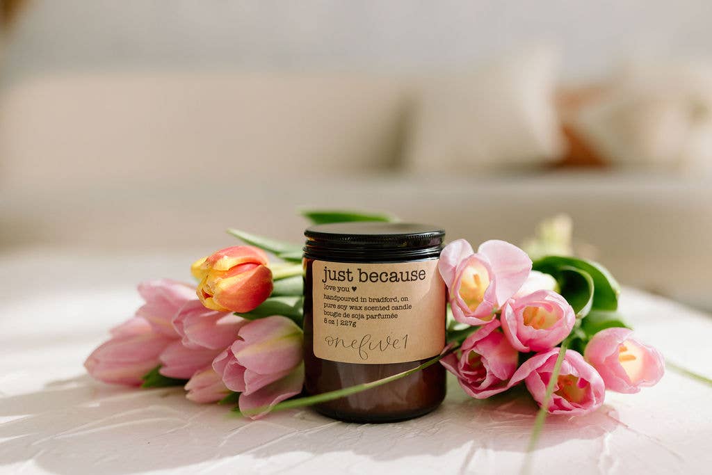 Candle labeled 'just because' with pink tulips on a soft surface