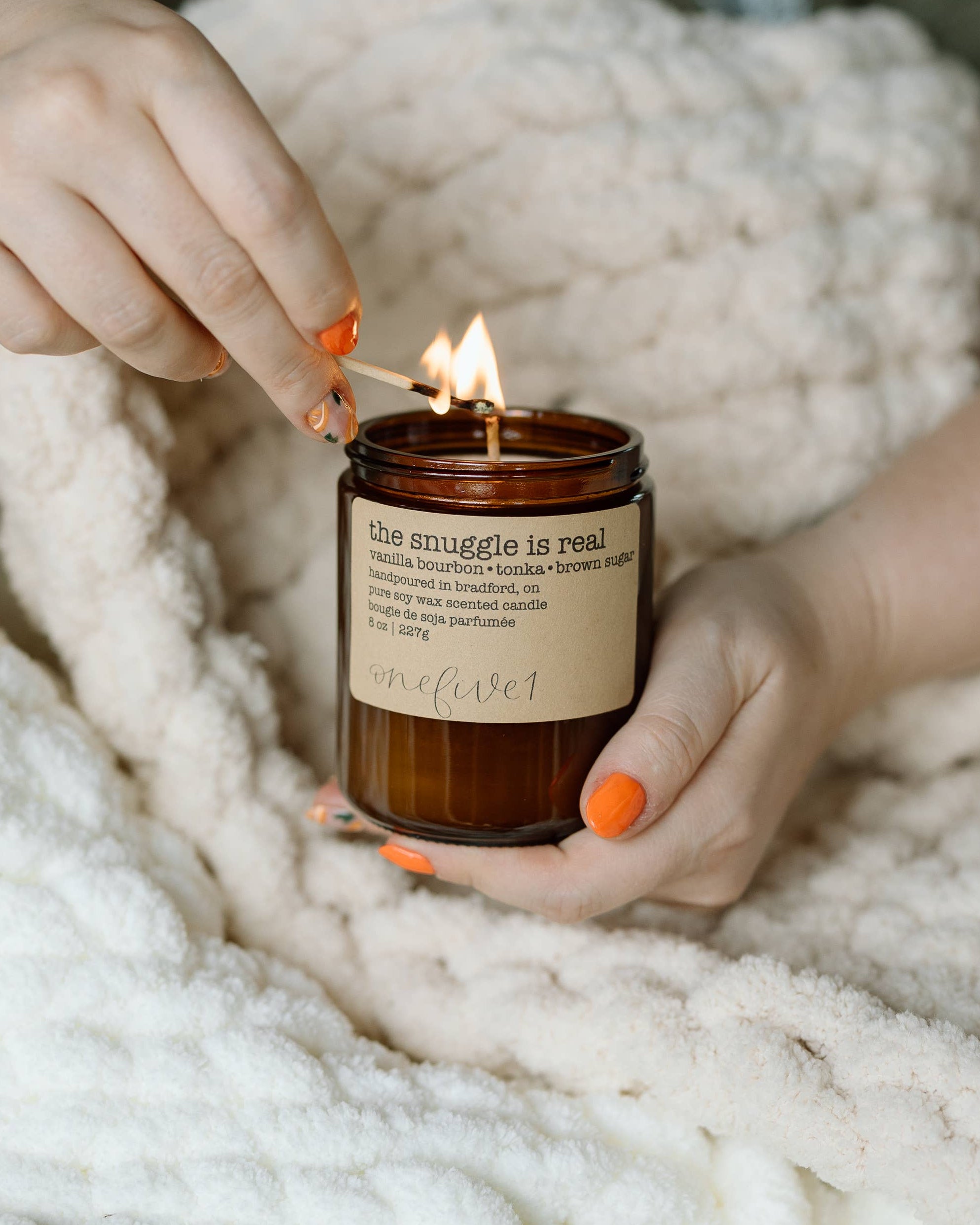 Person holding a lit candle wrapped in a cozy blanket