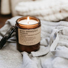 Candle in a glass jar with a label on a grey sweatpant surface