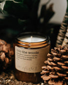 Candle labeled 'Into the Woods' surrounded by pine cones and plants