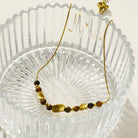 Hackney jewelry featuring a snake skin textured chain necklace with gold and tiger eye stone charms. 