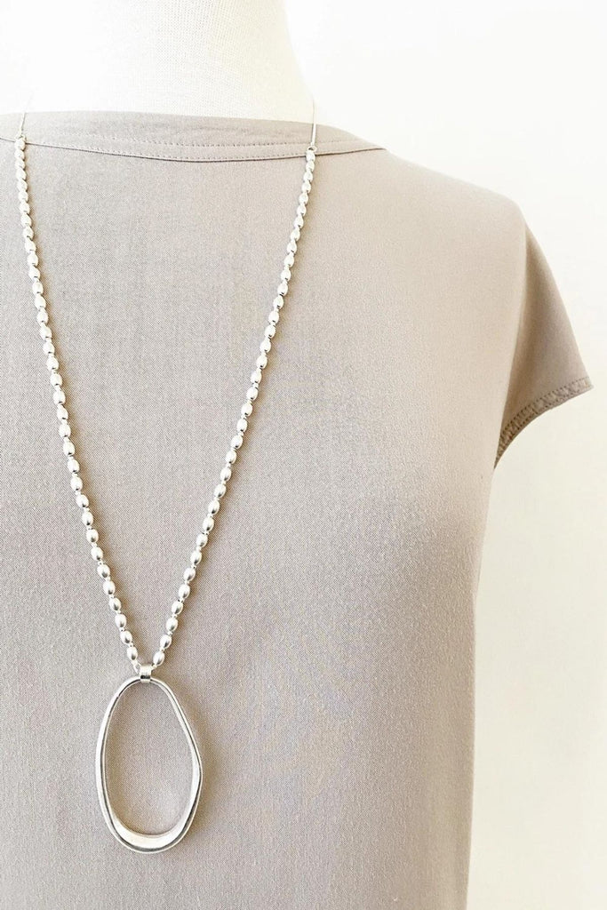 Caracol jewelry featuring a long adjustable necklace on flat chain with worn metal oval pendant