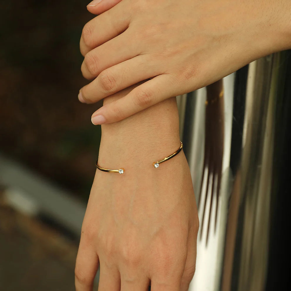 Hackney jewelry featuring an open adjustable gold bracelet with a gemstone on either opening end. 